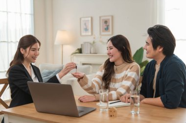 Emlakçı ev anahtarlarını müşteriye veriyor. Asyalı kadın emlakçı ev modeliyle aynı masada otururken alıcıya anahtarları veriyor. Gayrimenkul, yeni mülk alımı, ipotek konsepti