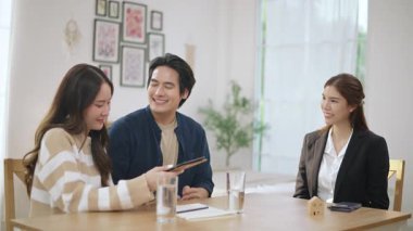 Asyalı finans danışmanı ofisteki genç çifte yeni proje yatırımını açıklıyor. Emlakçı aileyle ipotek seçeneklerini tartışıyor. Finans danışmanıyla ipotek kredisi danışmanlığı.