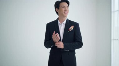 Siyah takım elbiseli bir damat kollarını düzeltirken özgüvenle gülümsüyor. Adam mutlu görünüyor. Düğün günü için hazırlanıyor. Aşk evliliği kutlamaları romantizm ve düğün hazırlıkları.