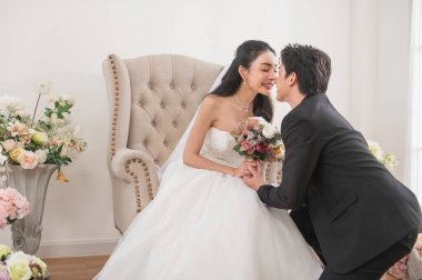 Damat diz çöker ve parlak bir stüdyoda çiçeklerle çevrili beyaz gelinliğiyle gülümseyen gelinine bir buket sunar. Mükemmel romantik düğün anı.