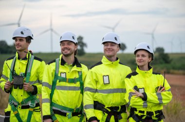 Güvenlik kaskı takan mühendisler rüzgar tarlasında rüzgar türbinlerini inceliyor. Takım çalışması yenilenebilir enerji, sürdürülebilir gelişme, temiz teknoloji çevre mühendisliği rüzgar enerjisi üretimi.