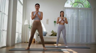 Evindeki oturma odasında çömelme hareketi yapan iki Asyalı kadın. sağlıklı alışkanlıklar, spor ve eğlence konsepti.