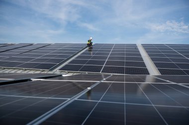 Teknisyen yeşil enerji için fabrikanın çatısına güneş panelleri kuruyor. Güvenlik teçhizatı konusunda yetenekli bir teknisyen çatıdaki bir güneş paneli tesisi üzerinde çalışıyor. Temiz enerji yenilenebilir enerji teknolojisi.