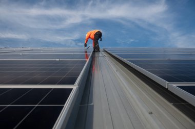 Teknisyen yeşil enerji için fabrikanın çatısına güneş panelleri kuruyor. Güvenlik teçhizatı konusunda yetenekli bir teknisyen çatıdaki bir güneş paneli tesisi üzerinde çalışıyor. Temiz enerji yenilenebilir enerji teknolojisi.