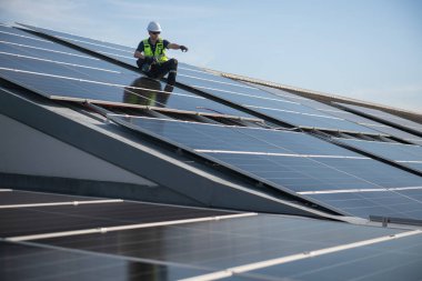Teknisyen yeşil enerji için fabrikanın çatısına güneş panelleri kuruyor. Güvenlik teçhizatı konusunda yetenekli bir teknisyen çatıdaki bir güneş paneli tesisi üzerinde çalışıyor. Temiz enerji yenilenebilir enerji teknolojisi.