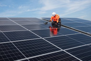 Teknisyen yeşil enerji için fabrikanın çatısına güneş panelleri kuruyor. Güvenlik teçhizatı konusunda yetenekli bir teknisyen çatıdaki bir güneş paneli tesisi üzerinde çalışıyor. Temiz enerji yenilenebilir enerji teknolojisi.