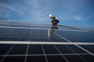 Teknisyen yeşil enerji için fabrikanın çatısına güneş panelleri kuruyor. Güvenlik teçhizatı konusunda yetenekli bir teknisyen çatıdaki bir güneş paneli tesisi üzerinde çalışıyor. Temiz enerji yenilenebilir enerji teknolojisi.