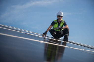 Teknisyen yeşil enerji için fabrikanın çatısına güneş panelleri kuruyor. Güvenlik teçhizatı konusunda yetenekli bir teknisyen çatıdaki bir güneş paneli tesisi üzerinde çalışıyor. Temiz enerji yenilenebilir enerji teknolojisi.