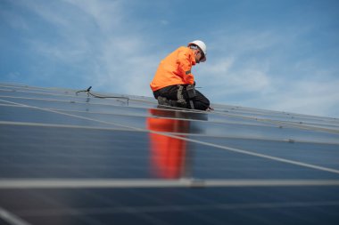 Teknisyen yeşil enerji için fabrikanın çatısına güneş panelleri kuruyor. Güvenlik teçhizatı konusunda yetenekli bir teknisyen çatıdaki bir güneş paneli tesisi üzerinde çalışıyor. Temiz enerji yenilenebilir enerji teknolojisi.