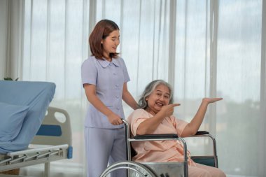 Hastane koğuşunda yaşlı kadın hastayı tekerlekli sandalyeye iten Asyalı hemşire, yaşlı bakım konsepti