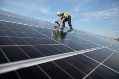 Teknisyen yeşil enerji için fabrikanın çatısına güneş panelleri kuruyor. Güvenlik teçhizatı konusunda yetenekli bir teknisyen çatıdaki bir güneş paneli tesisi üzerinde çalışıyor. Temiz enerji yenilenebilir enerji teknolojisi.
