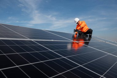 Teknisyen yeşil enerji için fabrikanın çatısına güneş panelleri kuruyor. Güvenlik teçhizatı konusunda yetenekli bir teknisyen çatıdaki bir güneş paneli tesisi üzerinde çalışıyor. Temiz enerji yenilenebilir enerji teknolojisi.