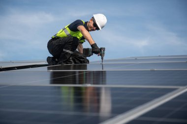 Teknisyen yeşil enerji için fabrikanın çatısına güneş panelleri kuruyor. Güvenlik teçhizatı konusunda yetenekli bir teknisyen çatıdaki bir güneş paneli tesisi üzerinde çalışıyor. Temiz enerji yenilenebilir enerji teknolojisi.