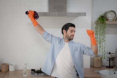 Modern bir mutfakta turuncu eldivenli bir adam temizlik yapıyor. Ev idaresi kavramları, ev bakımına adanmışlık ve temiz ve sağlıklı bir ev ortamı sağlama çabaları..