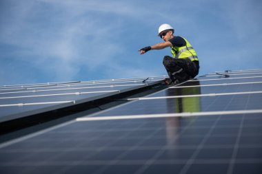 Teknisyen yeşil enerji için fabrikanın çatısına güneş panelleri kuruyor. Güvenlik teçhizatı konusunda yetenekli bir teknisyen çatıdaki bir güneş paneli tesisi üzerinde çalışıyor. Temiz enerji yenilenebilir enerji teknolojisi.