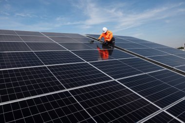 Teknisyen yeşil enerji için fabrikanın çatısına güneş panelleri kuruyor. Güvenlik teçhizatı konusunda yetenekli bir teknisyen çatıdaki bir güneş paneli tesisi üzerinde çalışıyor. Temiz enerji yenilenebilir enerji teknolojisi.