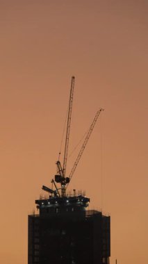 Gün batımında yüksek binalarda çalışan vinçlerin zaman çizelgesi..