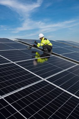 Teknisyen yeşil enerji için fabrikanın çatısına güneş panelleri kuruyor. Güvenlik teçhizatı konusunda yetenekli bir teknisyen çatıdaki bir güneş paneli tesisi üzerinde çalışıyor. Temiz enerji yenilenebilir enerji teknolojisi.