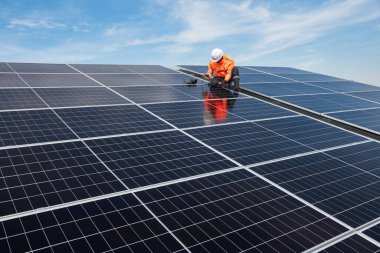 Teknisyen yeşil enerji için fabrikanın çatısına güneş panelleri kuruyor. Güvenlik teçhizatı konusunda yetenekli bir teknisyen çatıdaki bir güneş paneli tesisi üzerinde çalışıyor. Temiz enerji yenilenebilir enerji teknolojisi.
