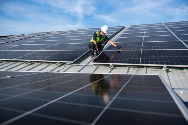 Teknisyen yeşil enerji için fabrikanın çatısına güneş panelleri kuruyor. Güvenlik teçhizatı konusunda yetenekli bir teknisyen çatıdaki bir güneş paneli tesisi üzerinde çalışıyor. Temiz enerji yenilenebilir enerji teknolojisi.