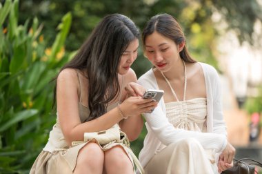 Gülümserken ve akıllı telefona bakarken yan yana oturan iki genç kadın. Sahne gerçek dostluğu, bağlılığı, mutluluğu ve paylaşılan deneyimleri yansıtıyor..
