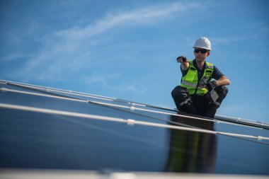 Teknisyen yeşil enerji için fabrikanın çatısına güneş panelleri kuruyor. Güvenlik teçhizatı konusunda yetenekli bir teknisyen çatıdaki bir güneş paneli tesisi üzerinde çalışıyor. Temiz enerji yenilenebilir enerji teknolojisi.