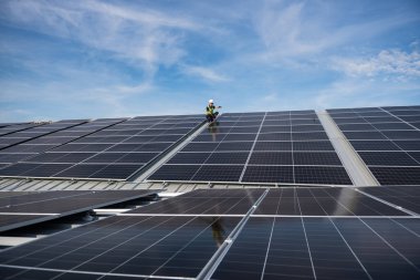Teknisyen yeşil enerji için fabrikanın çatısına güneş panelleri kuruyor. Güvenlik teçhizatı konusunda yetenekli bir teknisyen çatıdaki bir güneş paneli tesisi üzerinde çalışıyor. Temiz enerji yenilenebilir enerji teknolojisi.