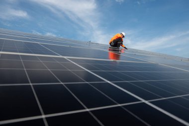 Teknisyen yeşil enerji için fabrikanın çatısına güneş panelleri kuruyor. Güvenlik teçhizatı konusunda yetenekli bir teknisyen çatıdaki bir güneş paneli tesisi üzerinde çalışıyor. Temiz enerji yenilenebilir enerji teknolojisi.