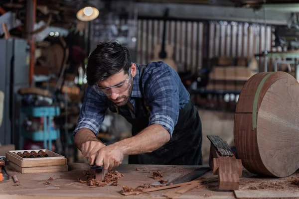 Ahşap işçisi, geleneksel bir aletle klasik gitar yaptığı için bileme taşında keski keskinleştirirken görülüyor..