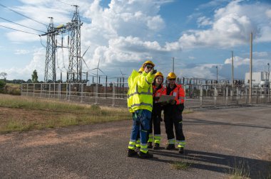 Elektrik santralinde çalışan mühendisler. Bir rüzgar türbini çiftliğindeki elektrik santralini denetleyen güvenlik kaskı takan teknisyen, elektrik ve sanayi çevresi için eko teknolojisi.