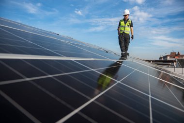 Teknisyen yeşil enerji için fabrikanın çatısına güneş panelleri kuruyor. Güvenlik teçhizatı konusunda yetenekli bir teknisyen çatıdaki bir güneş paneli tesisi üzerinde çalışıyor. Temiz enerji yenilenebilir enerji teknolojisi.