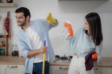 Mutlu genç çift modern mutfaklarını temizleyip sterilize ederken eğleniyor. Modern mutfakta duruyor. Ellerinde temizlik malzemeleri ve koruyucu eldivenler vardı. Temizlik hijyenik ev hayatı.