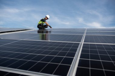 Teknisyen yeşil enerji için fabrikanın çatısına güneş panelleri kuruyor. Güvenlik teçhizatı konusunda yetenekli bir teknisyen çatıdaki bir güneş paneli tesisi üzerinde çalışıyor. Temiz enerji yenilenebilir enerji teknolojisi.
