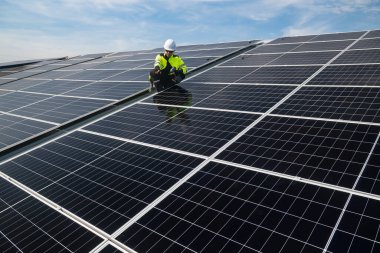 Teknisyen yeşil enerji için fabrikanın çatısına güneş panelleri kuruyor. Güvenlik teçhizatı konusunda yetenekli bir teknisyen çatıdaki bir güneş paneli tesisi üzerinde çalışıyor. Temiz enerji yenilenebilir enerji teknolojisi.