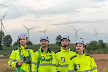 Güvenlik kaskı takan mühendisler rüzgar tarlasında rüzgar türbinlerini inceliyor. Takım çalışması yenilenebilir enerji, sürdürülebilir gelişme, temiz teknoloji çevre mühendisliği rüzgar enerjisi üretimi.