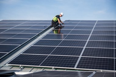 Teknisyen yeşil enerji için fabrikanın çatısına güneş panelleri kuruyor. Güvenlik teçhizatı konusunda yetenekli bir teknisyen çatıdaki bir güneş paneli tesisi üzerinde çalışıyor. Temiz enerji yenilenebilir enerji teknolojisi.