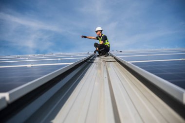 Teknisyen yeşil enerji için fabrikanın çatısına güneş panelleri kuruyor. Güvenlik teçhizatı konusunda yetenekli bir teknisyen çatıdaki bir güneş paneli tesisi üzerinde çalışıyor. Temiz enerji yenilenebilir enerji teknolojisi.