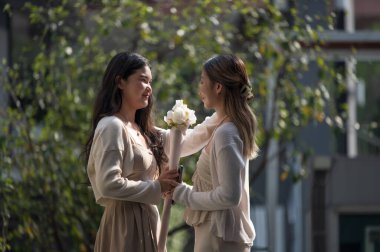 Happy Lesbian Couple Smiling at Each Other or two Close Female Friends Sharing a Happy Moment with Flowers. Ideal for concepts of queer love anniversaries or special celebrations.