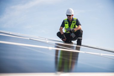 Teknisyen yeşil enerji için fabrikanın çatısına güneş panelleri kuruyor. Güvenlik teçhizatı konusunda yetenekli bir teknisyen çatıdaki bir güneş paneli tesisi üzerinde çalışıyor. Temiz enerji yenilenebilir enerji teknolojisi.