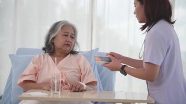 Genç Asyalı hemşire hastane koğuşundaki yaşlı kadın hastaya kahvaltı hazırlıyor..