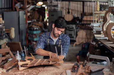Luthier bir gitar yaratıyor ve geleneksel olarak aletleri kullanıyor. Yapım aşamasında olan bir gitarın gövdesine kelepçe takıyor. Yapıştırıcı yapışkanlığını geliştiriyor..