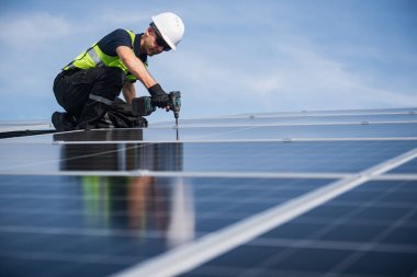 Teknisyen yeşil enerji için fabrikanın çatısına güneş panelleri kuruyor. Güvenlik teçhizatı konusunda yetenekli bir teknisyen çatıdaki bir güneş paneli tesisi üzerinde çalışıyor. Temiz enerji yenilenebilir enerji teknolojisi.