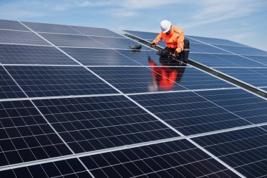 Teknisyen yeşil enerji için fabrikanın çatısına güneş panelleri kuruyor. Güvenlik teçhizatı konusunda yetenekli bir teknisyen çatıdaki bir güneş paneli tesisi üzerinde çalışıyor. Temiz enerji yenilenebilir enerji teknolojisi.