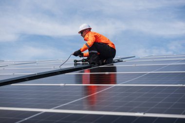 Teknisyen yeşil enerji için fabrikanın çatısına güneş panelleri kuruyor. Güvenlik teçhizatı konusunda yetenekli bir teknisyen çatıdaki bir güneş paneli tesisi üzerinde çalışıyor. Temiz enerji yenilenebilir enerji teknolojisi.