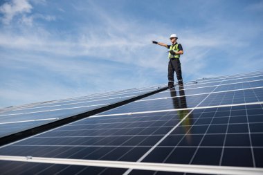 Teknisyen yeşil enerji için fabrikanın çatısına güneş panelleri kuruyor. Güvenlik teçhizatı konusunda yetenekli bir teknisyen çatıdaki bir güneş paneli tesisi üzerinde çalışıyor. Temiz enerji yenilenebilir enerji teknolojisi.