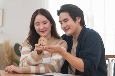 Mutlu Asyalı aile genç çiftimiz ellerinde model evlerle yeni bir ev almak için para biriktirmenin anahtarlarını gösteriyorlar. İş finansmanı, finansal planlama için banka mevduatı.