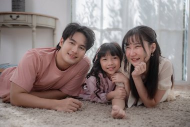 Mutlu Asyalı bir aile yerde uzanıyor ve evde birlikte gülümsüyor, ebeveynler ve kızlar kaliteli vakit geçiriyorlar. Aile mutluluğu, bağlılık, ebeveynlik ve neşeli ev hayatı kavramı.