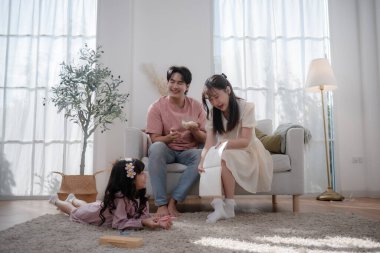 Mutlu Asyalı aile evde birlikte vakit geçiriyor ebeveynler küçük kızlarını oturma odasında resim çizerken izliyor. Aile bağı, ebeveynlik, yaratıcılık, evde öğrenme, mutluluk.