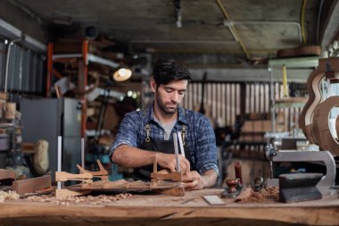 Luthier bir gitar yaratıyor ve geleneksel olarak aletleri kullanıyor. Yapım aşamasında olan bir gitarın gövdesine kelepçe takıyor. Yapıştırıcı yapışkanlığını geliştiriyor..
