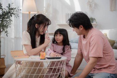 Mutlu Asyalı aile kızlarıyla birlikte eğleniyor ve birlikte ders çalışıyor, ebeveynler ve kızları oturma odasında kaliteli vakit geçiriyorlar, birlikte öğreniyorlar ve oynuyorlar. Aile bağı, ebeveynlik, eğitim ve aşk.